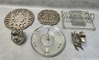 Full lot overview showing six silver plated items: two duck figurines, two round trivets, one round tiered tray, one toast/letter rack