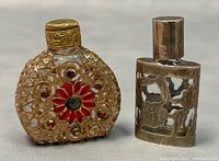 Photo showing front view of two vintage glass perfume bottles: one with sterling silver overlay and red enamel flower with rhinestones, the other with gold-tone detailing and Czech rhinestones.