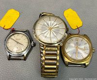 Three vintage watches including a Cardinal, Tissot, and another watch on gray surface with yellow tags.