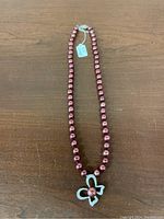Full length view of red pearl bead necklace with silver bow pendant on wooden surface.