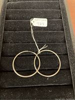 Pair of sterling silver round hoop earrings lying on black padded jewelry holder with tag showing 'Stamped 925'