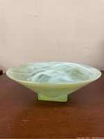 Side angle view of the green and white swirled art glass bowl on a wood surface, showing shape and base.