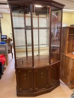 Front view of wooden curio cabinet with glass shelves and lower wooden doors.