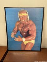 Framed poster of Hulk Hogan in yellow wrestling attire, signed in lower right corner.