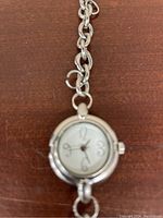 Close-up of the round watch face with Arabic numerals 3, 6, 9, and 12, silver-tone bezel, and small crown at 3 o'clock.