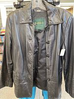 Front view of black leather ladies coat with button closure and collar on hanger.