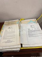 Photo showing two stacks of nautical and survey maps with text sheets on top describing different lakes and their survey data.