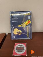 Sealed DVD for beginner acoustic guitar lessons with nylon strings and pick in the same image.