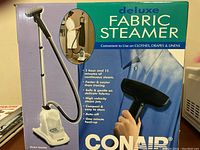 Photo of retail box showing the Conair Deluxe Fabric Steamer with model GS10RC, highlighting its use on clothes, drapes, and linens.