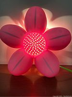 Pink flower-shaped IKEA Blomma vintage wall lamp illuminated on a surface, showing light diffusion through perforated center and translucent petals.