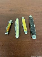 Four pocket knives displayed on table: small multicolored amber-tone handle knife, cream-colored Imperial Prime Cut knife, yellow handle knife, and largest dark textured handle knife.