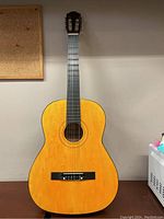 Front view of the Sakura junior acoustic guitar showing natural wood color and black bridge, six nylon strings with one string missing or needing replacement.