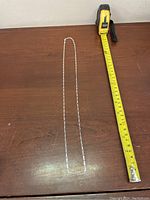 Full length of the silver chain necklace laid next to a tape measure showing approximately 24 inches long.