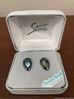 Pair of Storrs Glacier Pearls stud earrings in original box showing bear paw print abalone inlay detail.