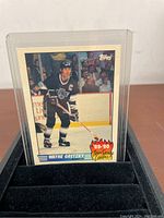 Front view of the Wayne Gretzky 1989-90 Topps Team Scoring Leaders hockey card displaying Gretzky in his Los Angeles Kings uniform on ice, in a protective clear sleeve.