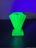 Green frosted uranium glass vase glowing bright green under UV light, showing geometric stepped design and square base from front view.