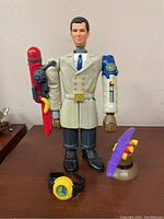 Front view of the Inspector Gadget action figure standing on a wooden surface with the helicopter propeller and wristwatch placed in front.