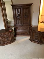 Photo of 42-inch armoire in dark wood with ornate carved doors and two lower drawers, flanked by two similarly styled end tables.
