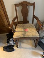 Front view of wooden armchair with floral cushioned seat, turned legs, and carved backrest.