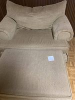 Beige fabric upholstered chair and matching ottoman placed together showing condition and size.