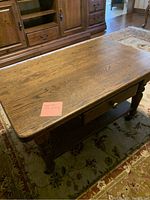 Full view of rectangular oak coffee table with a drawer and lower shelf, sitting on a patterned rug in front of a wooden cabinet.