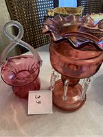 Two cranberry-colored glass figurines: a basket with twisted handle and ruffled-top vase with clear glass accents
