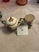 Photo showing a cream and sugar set made of ceramic with green and red floral decorations.