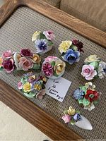 Photo showing 8 Crown Royal porcelain flower figurines arranged on a woven surface with a wooden frame border.