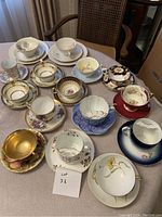 View of 11 assorted porcelain cups and matching saucers displayed on a table, showcasing floral and patterned decorations in various colors.