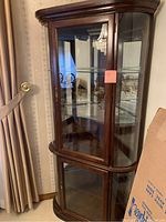Full front view of the corner curio cabinet showing its wood frame and glass doors with shelves inside.