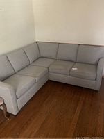 Full view of L-shaped grey fabric sectional sofa with cushions, right-angle design, positioned on hardwood floor near wall.