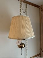 Brass hanging lamp with beige pleated shade hanging from brass chain, pull chain switch visible.