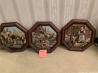 Shows three octagonal needle point pictures in wooden frames with pastoral and village themes.