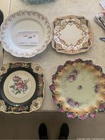 Top-down clear photo of four assorted decorative ceramic plates on a light surface, showing their patterns and shapes.