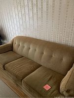 Front-side angle view of beige sofa showing button tufted backrest, seat cushions, and armrest.