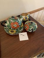 Tea set consisting of teapot, creamer, sugar bowl with lid, and three plates with bright floral hand-painted design.