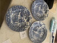 Top view showing three plates with detailed blue and white scenic design, laid on beige surface