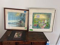 Overall lot view showing two framed artworks and one tile on table