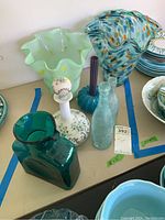 Overview of multiple art glass pieces on table with color variety and shapes including vases, bottles, and decanter