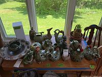 Wide view of the table displaying ceramic chickens, frogs, bird figurine, and decorative pottery bowls along with other ceramic items.