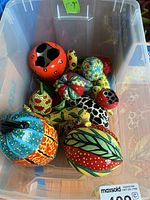 Overhead view of clear plastic bin containing assorted hand-painted ceramic fruit and vegetable pieces