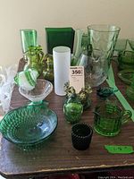 Various green art glass pieces including pitchers, vases, votives, paperweights, and a hobnail trinket dish arranged on a wooden table.