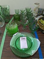 Full lot view showing green depression glass plates, bowls, stemmed glasses, ashtrays, and other glassware arranged on table.