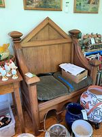 Front and angled view of the wooden pew bench, showing the triangular backrest design, armrests with rounded finials, and green cushions on the seat with visible wear and stain marks.