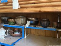 Shelf view of six ceramic and metal planters with varying designs and shapes.