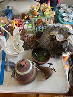 Overview of table with plush owl, wooden and metal pieces, ceramics and floral decor