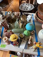 Overview of table with mixed ceramic items, glass bottles, terracotta figurines and rusted metal piece