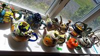 Full view of the set of 13 colorful decorative ceramic teapots on a windowsill showing variety in size and designs.