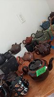 Overview of multiple decorative teapots arranged on wooden surface against white wall