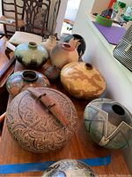 Wide shot of seven pottery and stoneware vessels on wooden table
